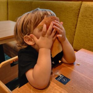 A young boy at a restaurant table holding a piece of bread to his face