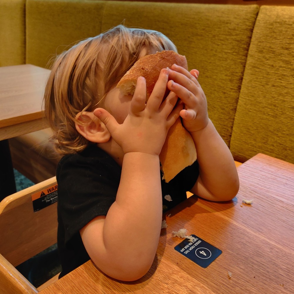 Damon at a restaurant table holding a piece of bread to his face.